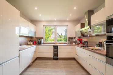 [Bungalov 4 kk s terasou - moderní kuchyň v bílé barvě s oknem do zahrady.]