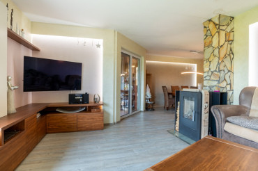 [Moderní obývací pokoj bungalovu 4 kk s terasou. Krbová kamna s kamenným obložením, průhled do kuchyně.]