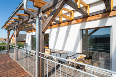 [Terasa moderní patrové dřevostavby od klíč od Haas. Terasa je částečně zakrytá.]