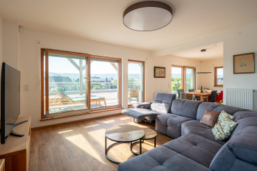 [Obývací pokoj moderní patrové dřevostavby na klíč od Haas. Prosklený interiér, minimalisticky zařízený obývací pokoj.]